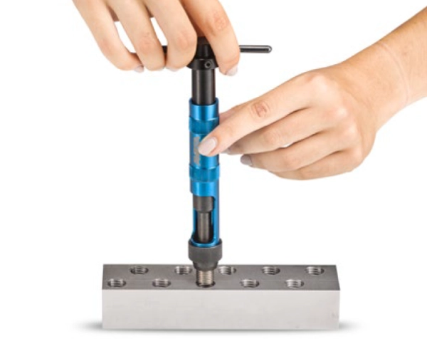 deux mains qui tiennent un outils de pose manuel pour installer un filet rapporté dans une pièce métallique